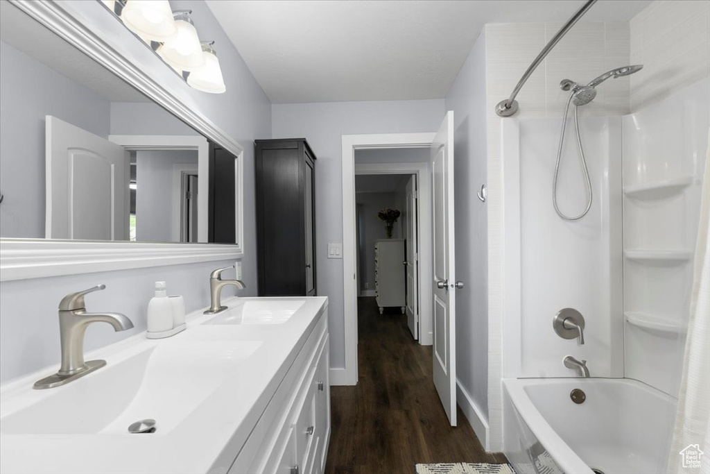 Full bathroom with shower / washtub combination, wood finished floors, double vanity, and baseboards