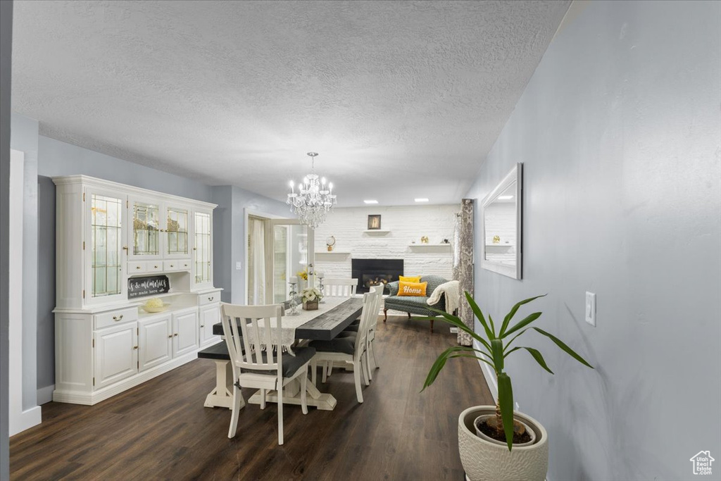 Dining space featuring a chandelier, dark wood-type flooring, a textured ceiling, a fireplace, and baseboards
