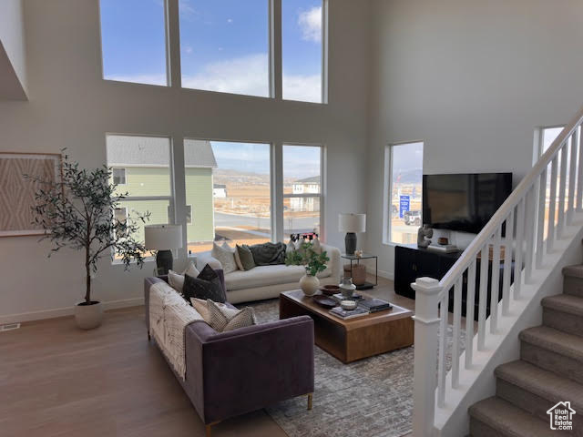Living area with stairs, wood finished floors, baseboards, and a high ceiling