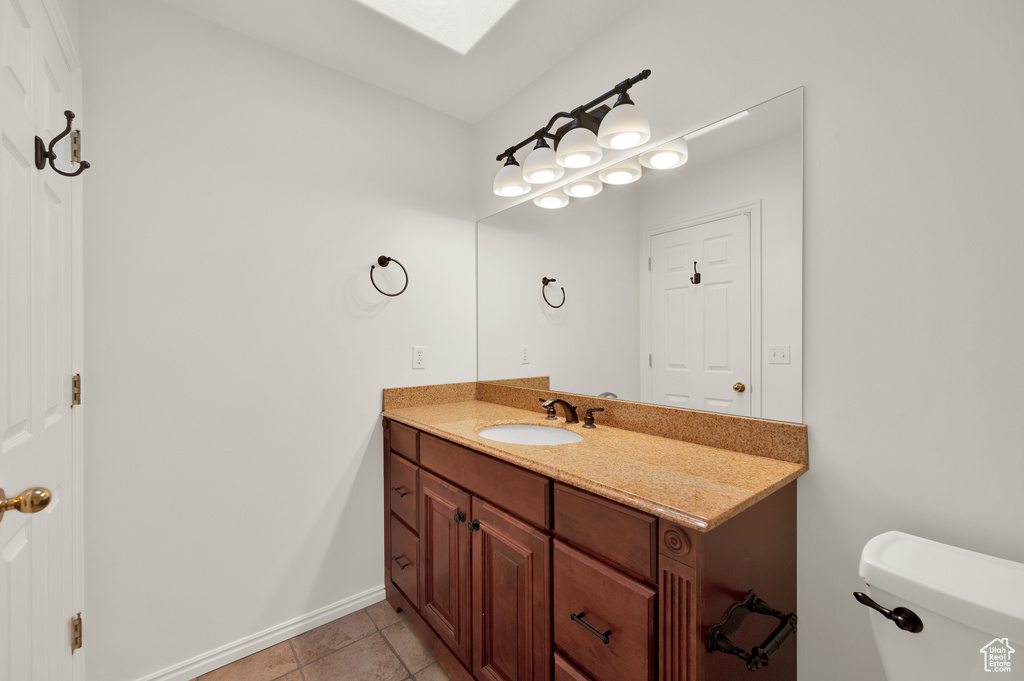 Bathroom featuring vanity, a skylight, toilet, tile patterned flooring, and baseboards