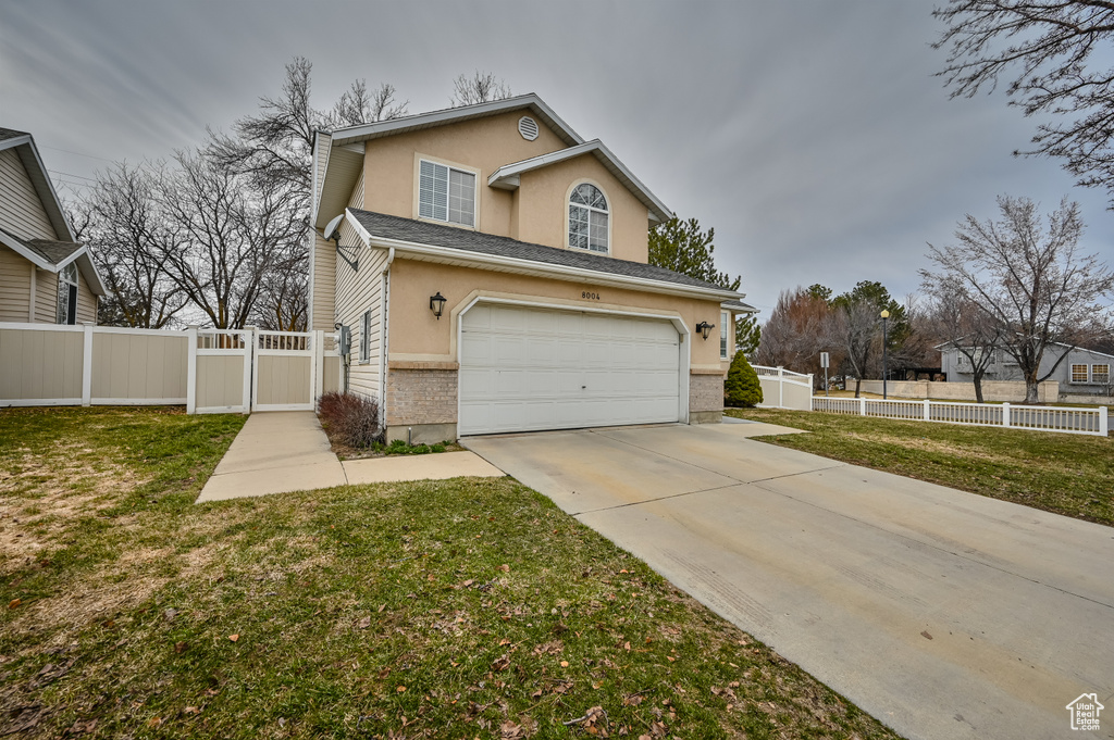 View of front of house with stucco siding, a gate, driveway, an attached garage, and brick siding