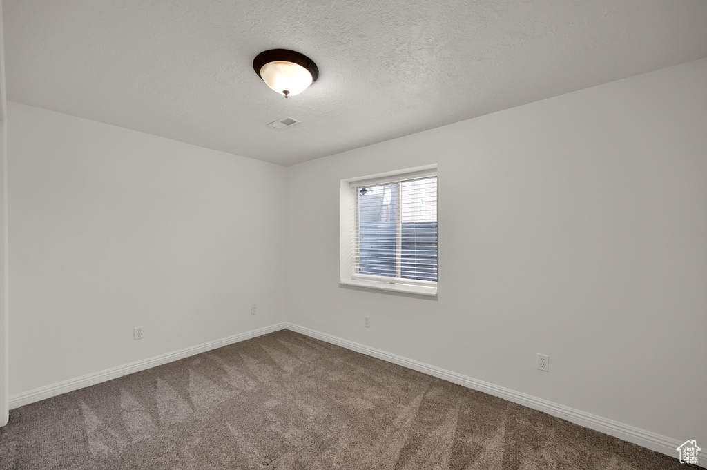 Empty room featuring dark carpet, baseboards, and a textured ceiling