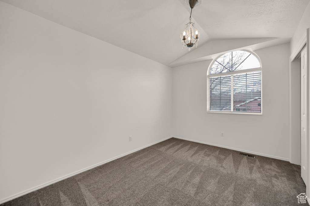 Unfurnished room featuring dark carpet, a chandelier, vaulted ceiling, and baseboards