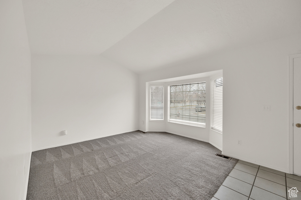 Spare room featuring vaulted ceiling, light tile patterned flooring, baseboards, and light colored carpet