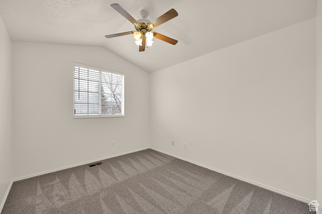 Empty room featuring dark carpet, ceiling fan, lofted ceiling, and baseboards