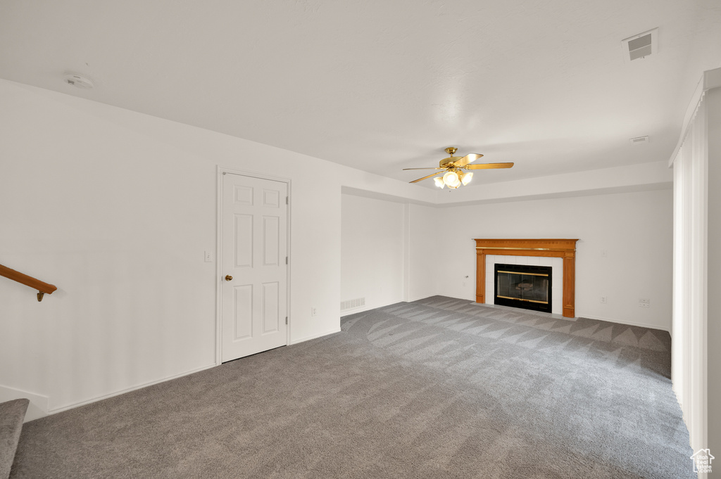 Unfurnished living room featuring carpet flooring, ceiling fan, a tiled fireplace, baseboards, and stairs