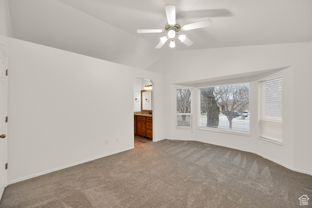 Carpeted empty room featuring a ceiling fan, vaulted ceiling, and baseboards
