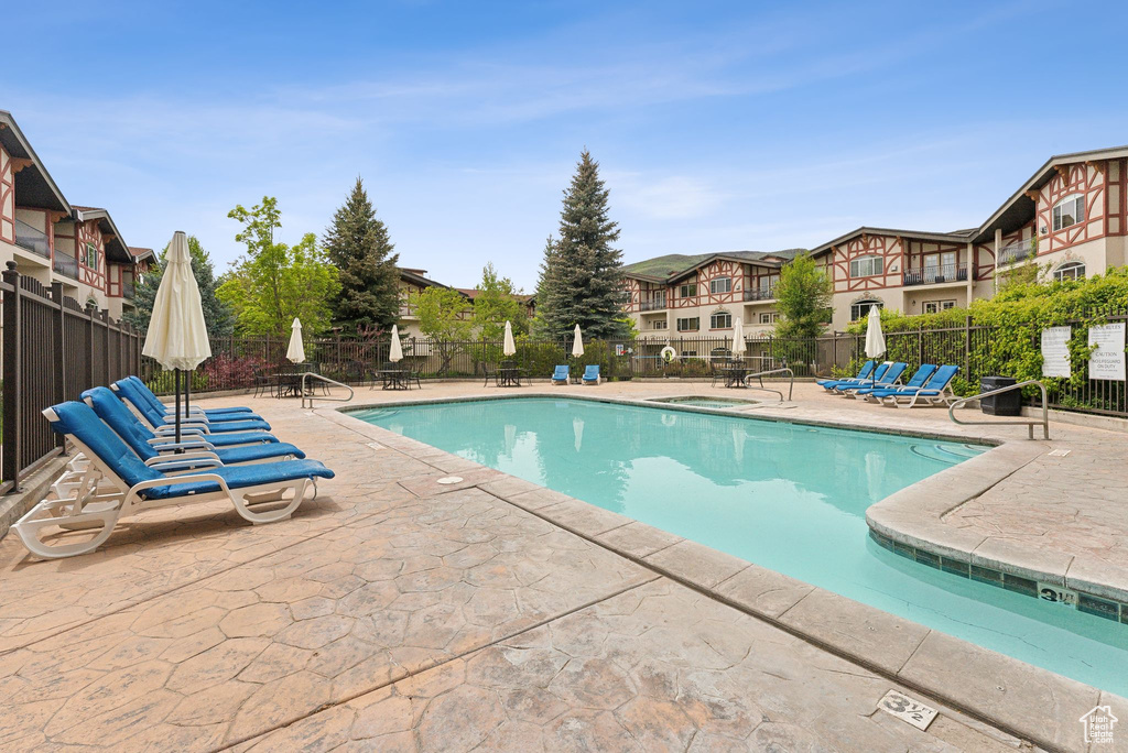 Community pool featuring a patio area, fence, a community hot tub, and a residential view