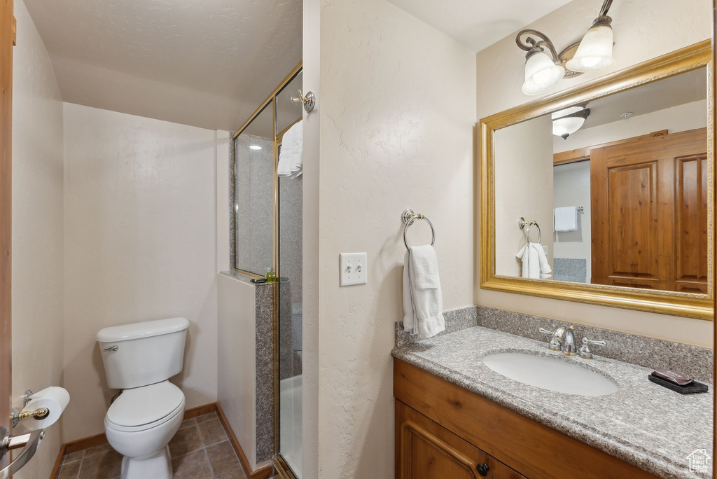 Bathroom featuring toilet, a stall shower, tile patterned floors, vanity, and baseboards