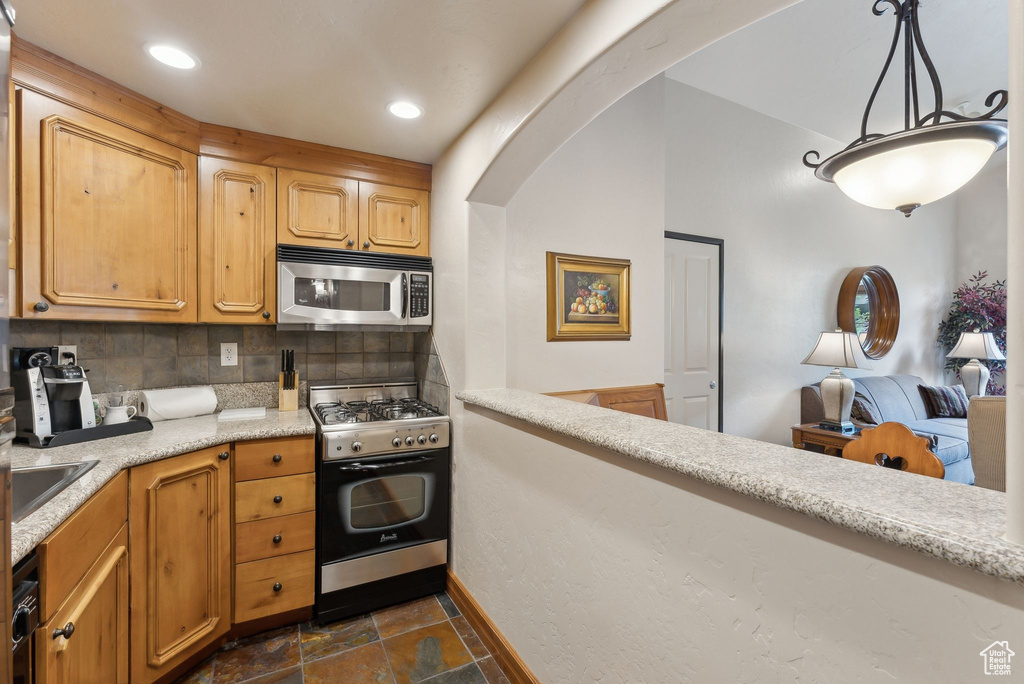 Kitchen featuring gas range, stainless steel microwave, stone tile floors, tasteful backsplash, and light countertops