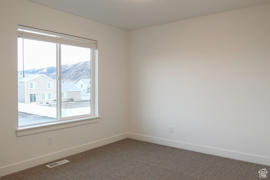 Empty room featuring healthy amount of natural light, dark colored carpet, and baseboards