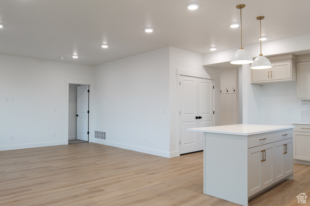 Kitchen featuring light wood finished floors, a kitchen island, light countertops, recessed lighting, and decorative light fixtures