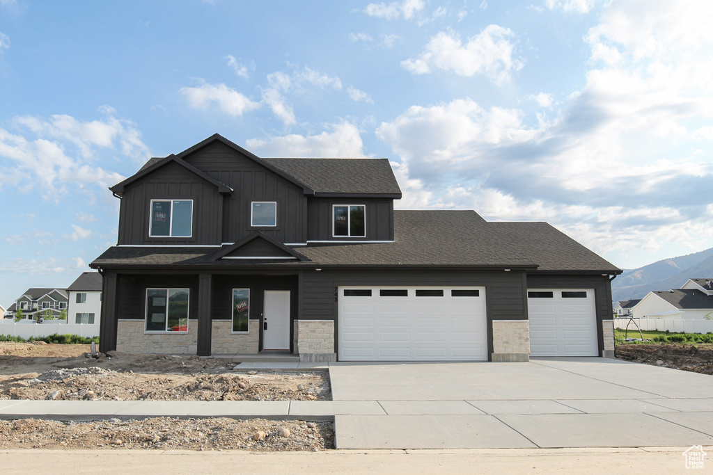 View of front facade featuring concrete driveway, a garage, stone siding, a mountain view, and roof with shingles