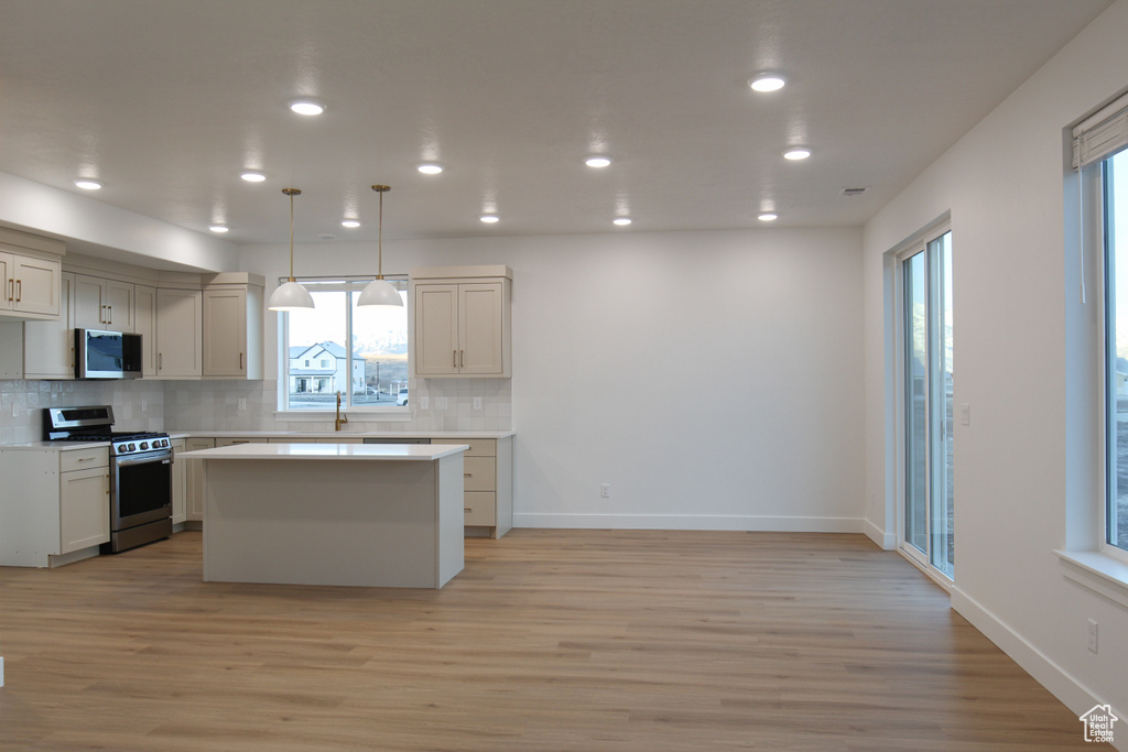 Kitchen with appliances with stainless steel finishes, a center island, light countertops, decorative backsplash, and light wood-style floors