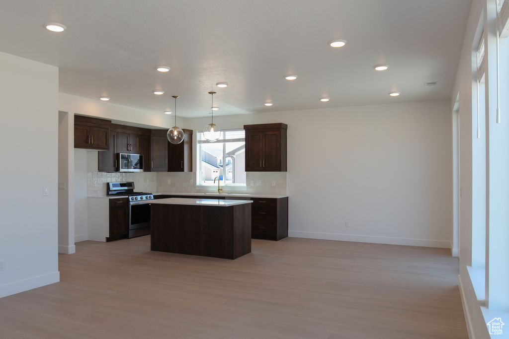 Kitchen featuring stainless steel gas stove, tasteful backsplash, a kitchen island, dark brown cabinets, and recessed lighting