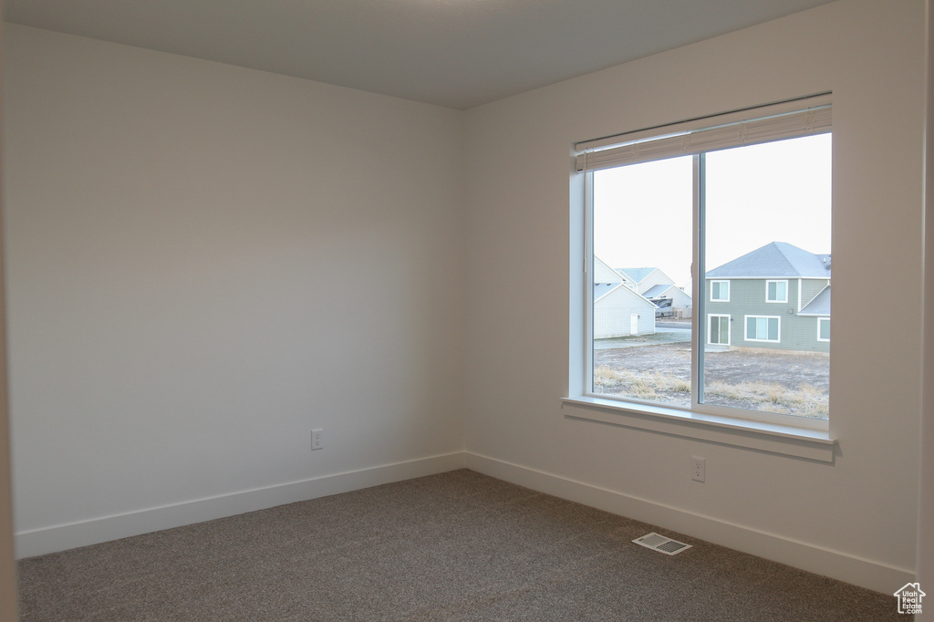 Spare room featuring healthy amount of natural light, baseboards, and dark colored carpet