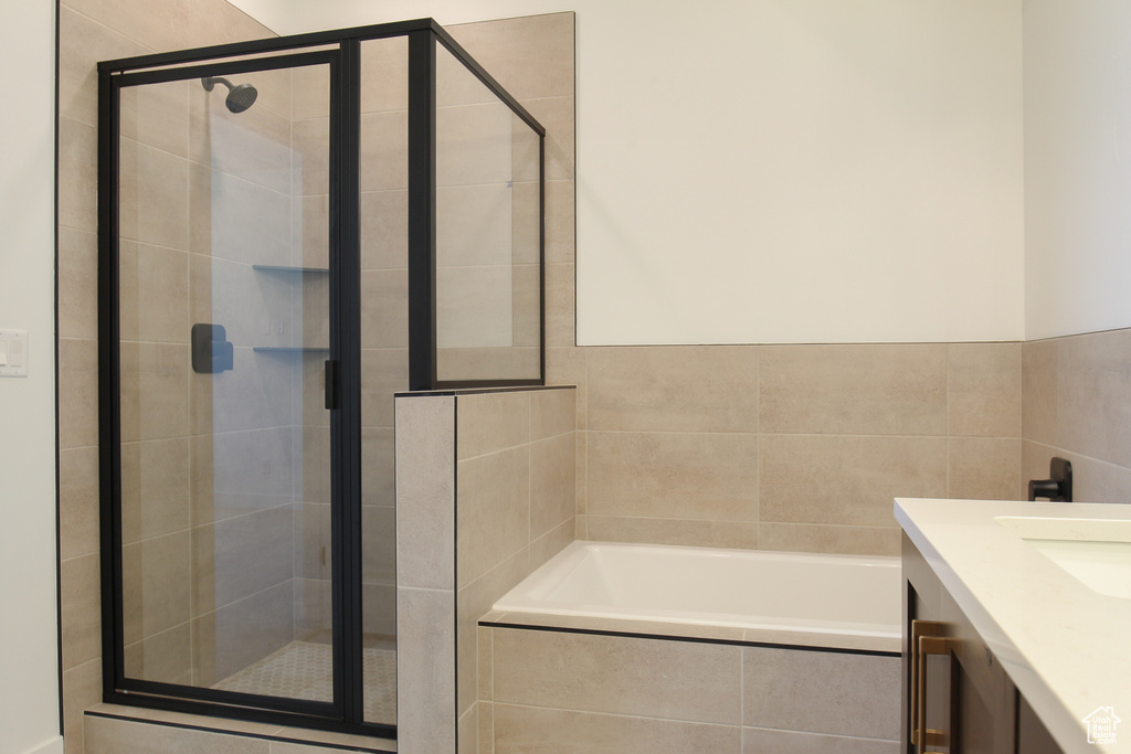 Bathroom with a garden tub, a stall shower, vanity, and tile walls