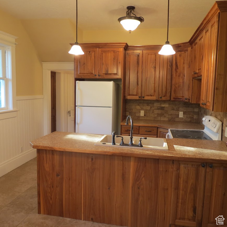 Kitchen with white appliances, brown cabinets, a peninsula, backsplash, and wainscoting