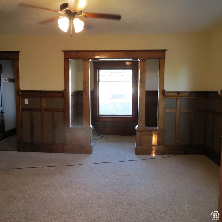 Unfurnished living room with carpet, ceiling fan, wainscoting, and a decorative wall