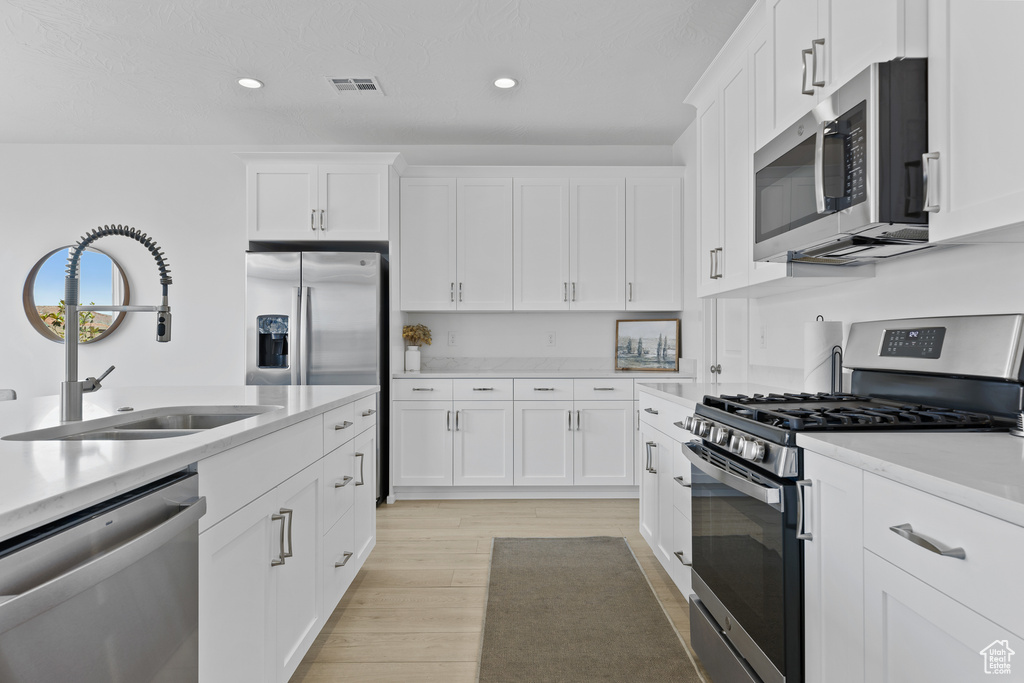 Kitchen featuring appliances with stainless steel finishes, a sink, recessed lighting, light wood-style flooring, and white cabinets