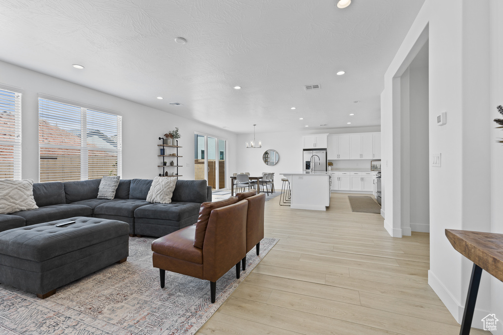 Living room featuring healthy amount of natural light, light wood-type flooring, recessed lighting, baseboards, and a chandelier