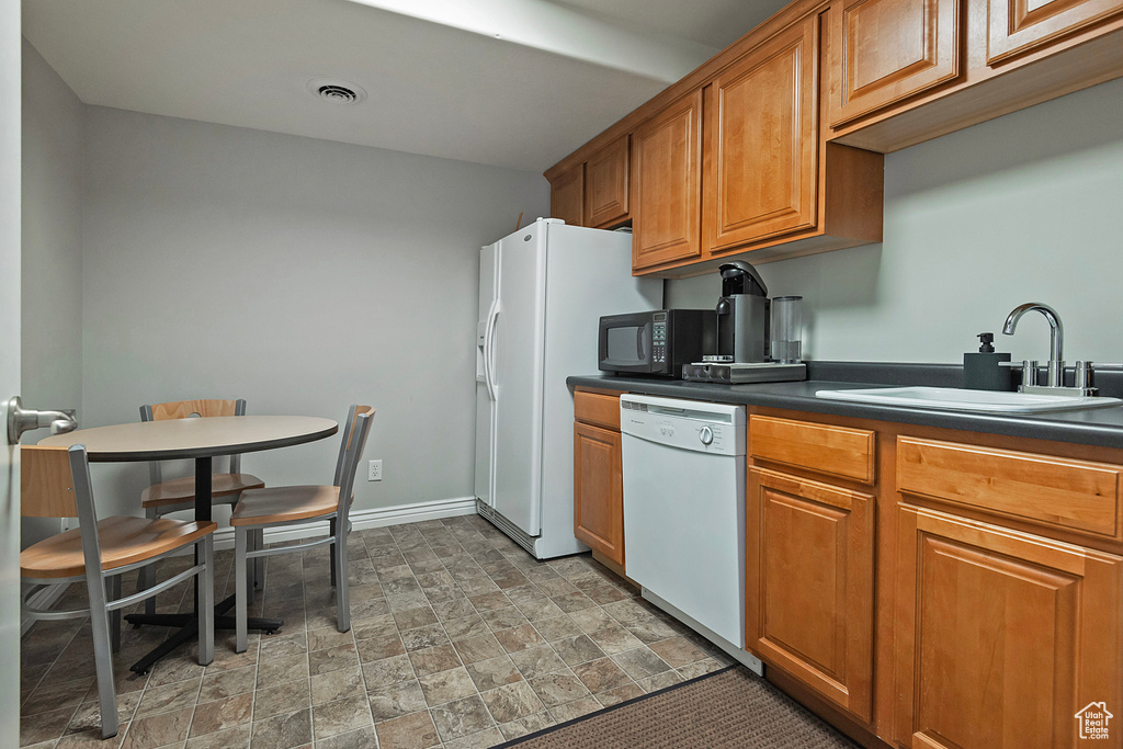 Kitchen with white appliances, a sink, dark countertops, brown cabinets, and stone finish flooring