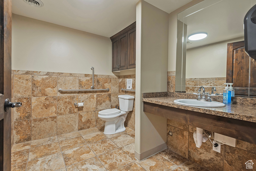 Bathroom featuring a sink, tile walls, toilet, a wainscoted wall, and stone tile floors