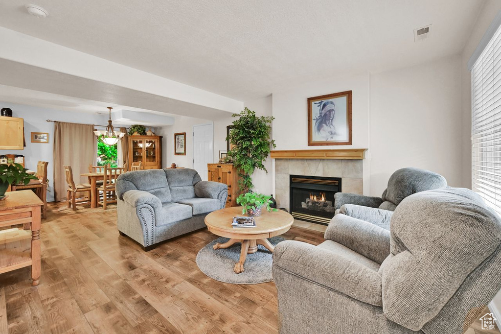 Living room with a tiled fireplace, a chandelier, and light wood-style floors