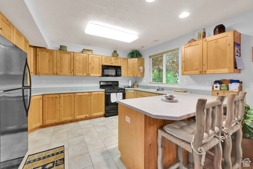 Kitchen featuring black appliances, a peninsula, light countertops, a breakfast bar, and a sink