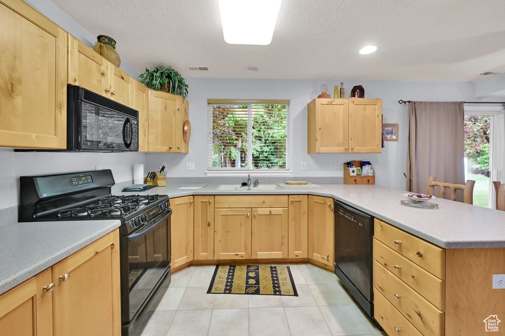 Kitchen with black appliances, light brown cabinets, a peninsula, a sink, and a textured ceiling