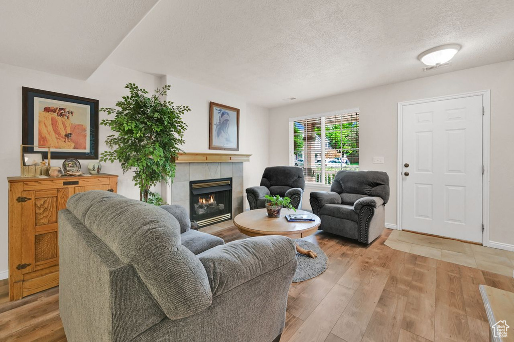 Living room with a textured ceiling, a tiled fireplace, light wood-type flooring, and baseboards