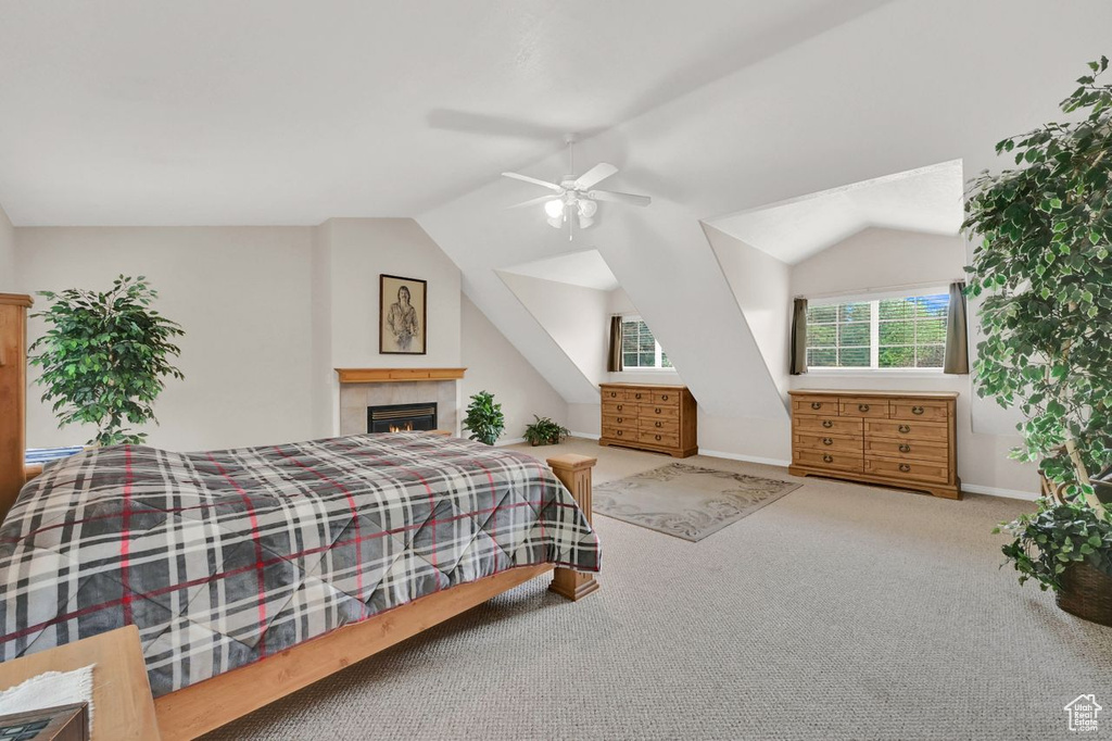 Carpeted bedroom featuring vaulted ceiling, baseboards, a fireplace, and a ceiling fan