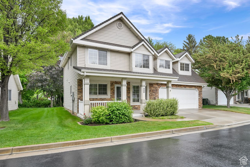 View of front of property with a porch, concrete driveway, a front lawn, stone siding, and an attached garage