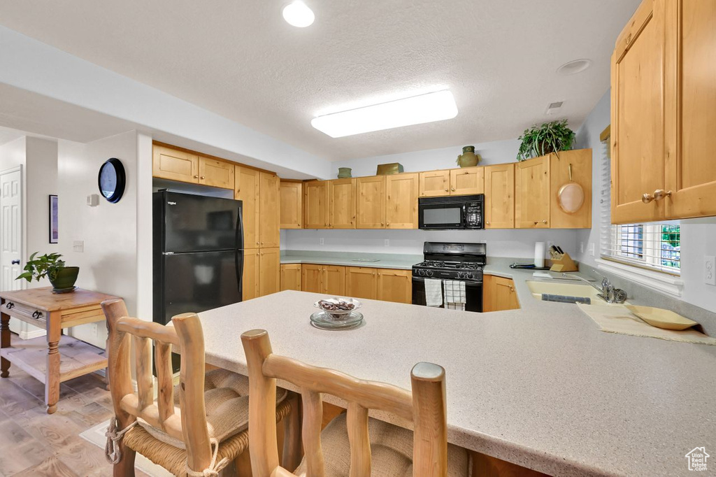 Kitchen featuring black appliances, a sink, a peninsula, light countertops, and light brown cabinets