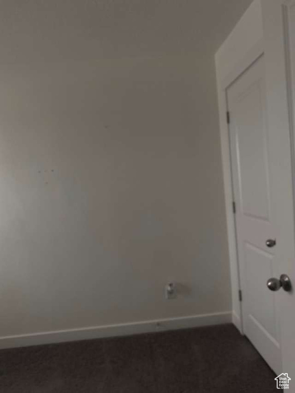 Spare room featuring baseboards and dark carpet