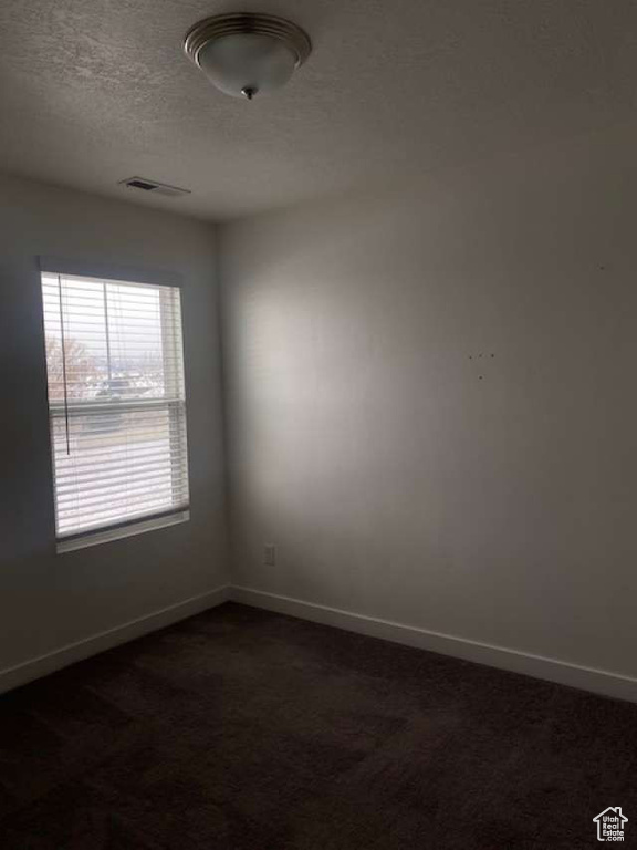 Spare room with baseboards, dark colored carpet, and a textured ceiling