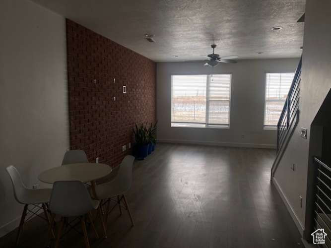Unfurnished dining area featuring baseboards, a ceiling fan, wood finished floors, brick wall, and an accent wall