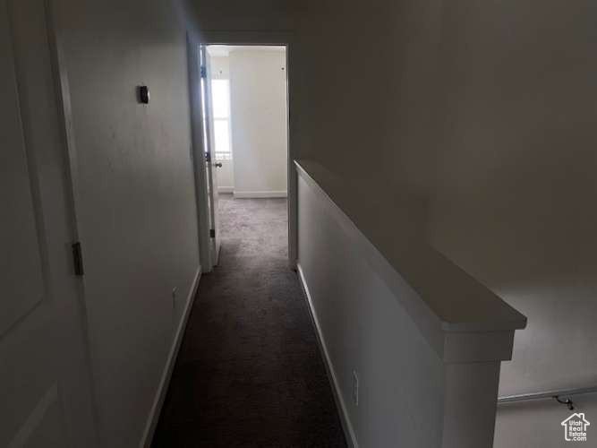 Corridor featuring dark colored carpet and baseboards