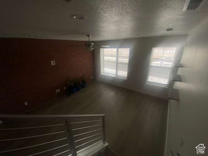 Spare room featuring a textured ceiling, wood finished floors, brick wall, and ceiling fan