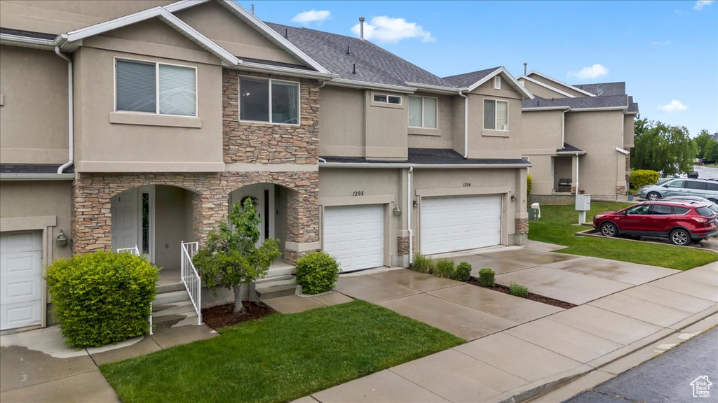 Townhome / multi-family property with stone siding, stucco siding, an attached garage, and driveway