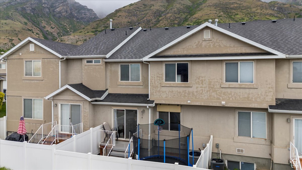 Back of property featuring stucco siding, roof with shingles, a fenced backyard, and a trampoline