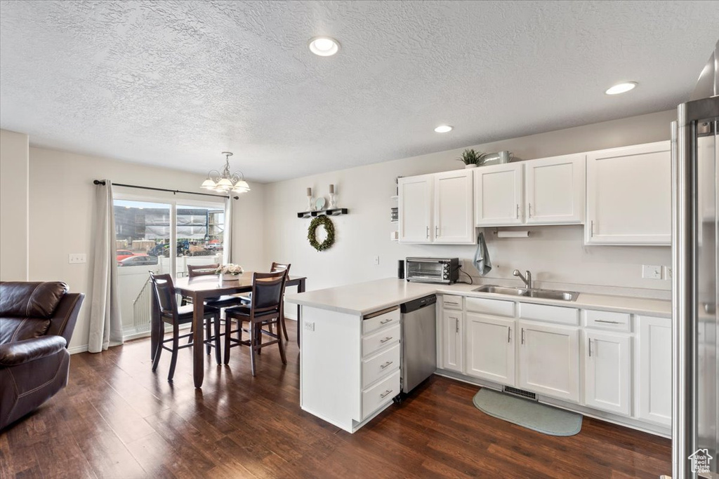 Kitchen featuring appliances with stainless steel finishes, a sink, a peninsula, a textured ceiling, and a chandelier