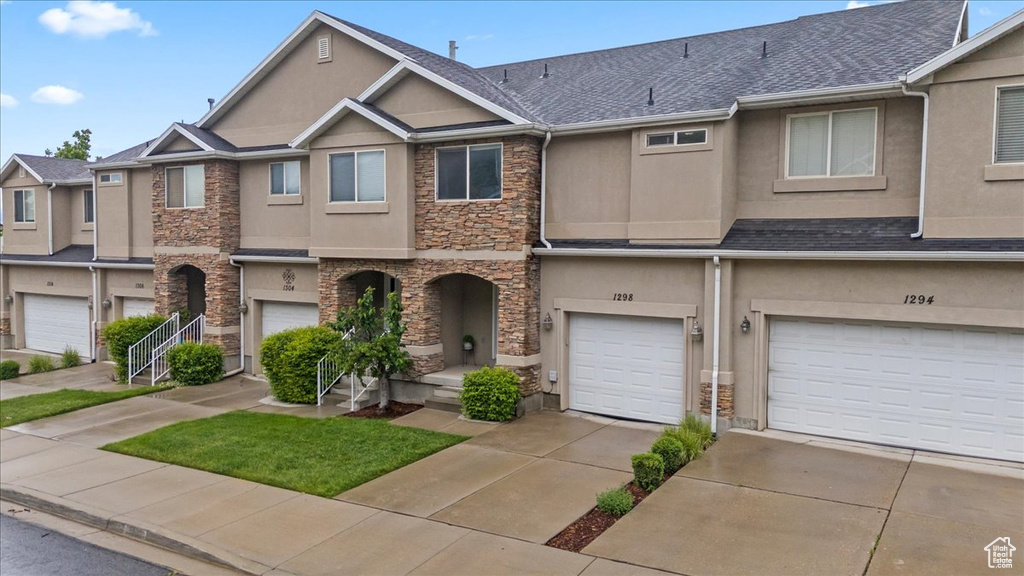 Townhome / multi-family property featuring stucco siding, stone siding, a garage, and driveway