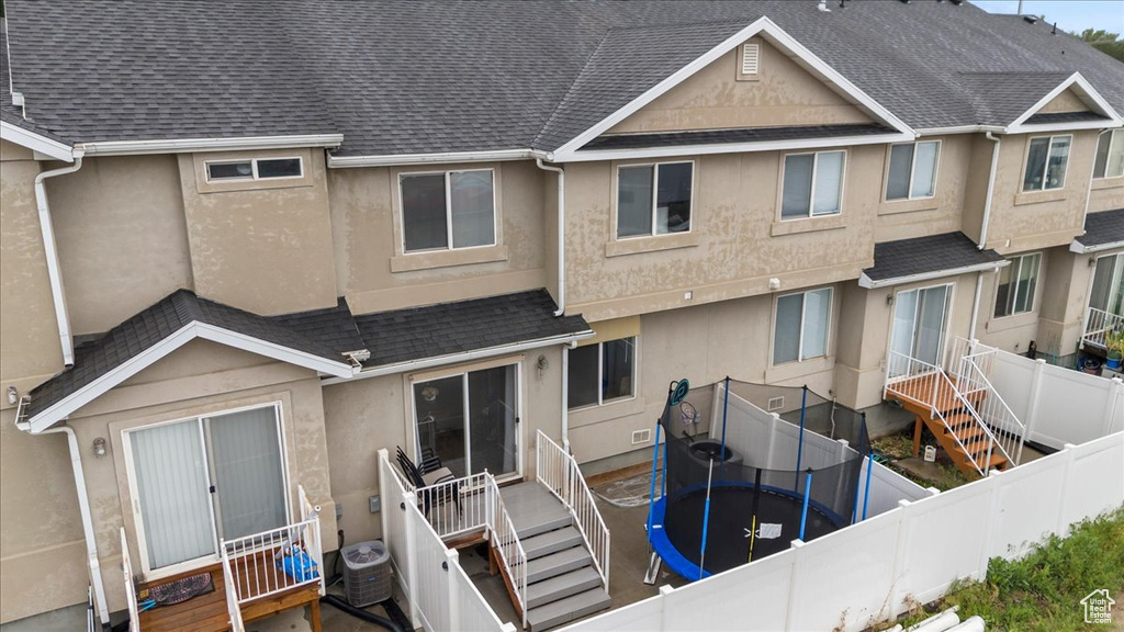 Rear view of property featuring a trampoline, stucco siding, and roof with shingles
