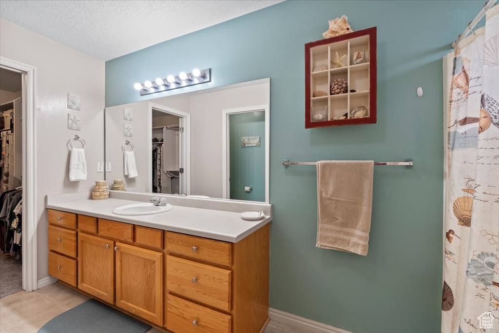 Bathroom featuring a walk in closet, vanity, tile patterned floors, and a textured ceiling