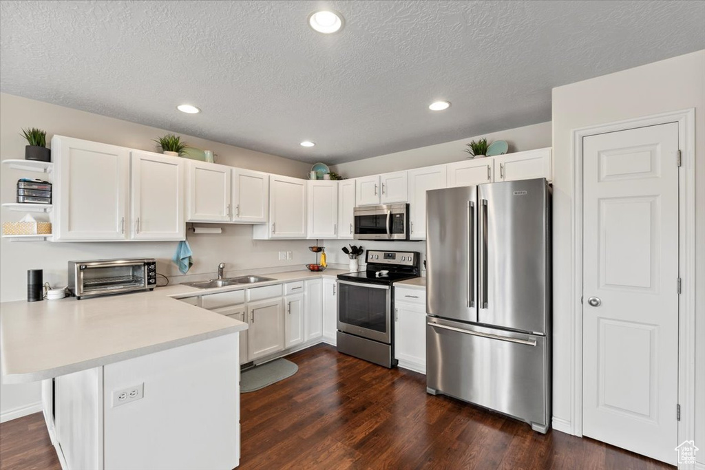 Kitchen featuring stainless steel appliances, a peninsula, a sink, light countertops, and white cabinetry