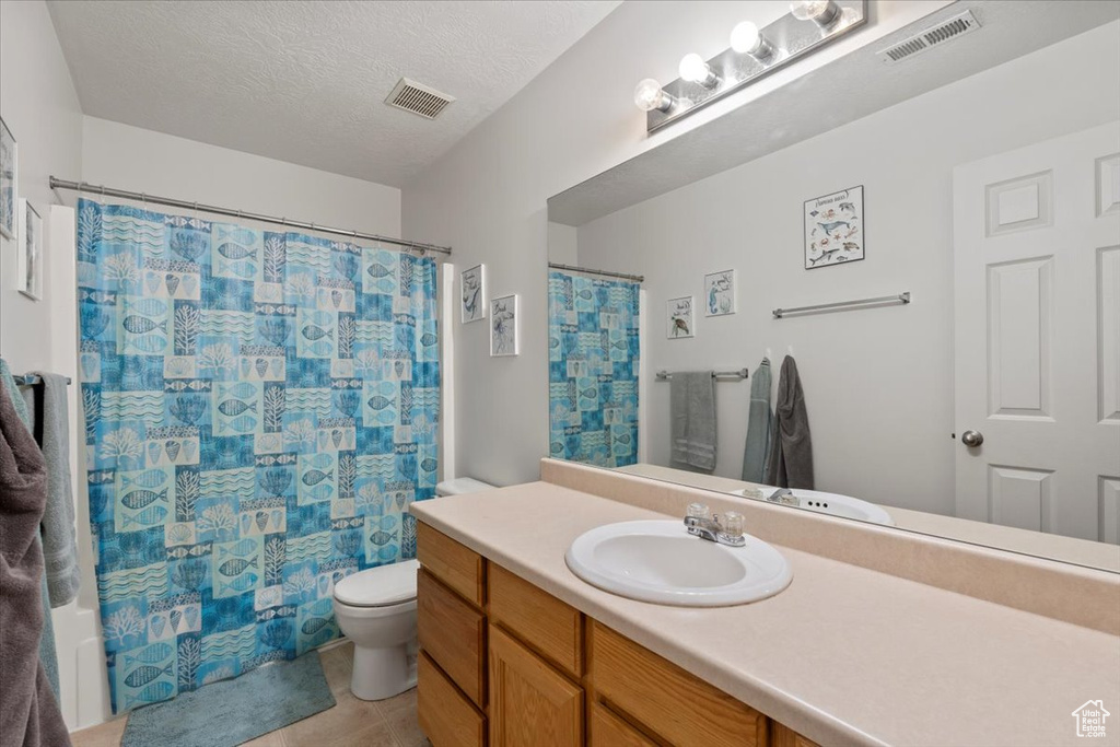 Bathroom featuring toilet, tile patterned flooring, vanity, a shower with curtain, and a textured ceiling