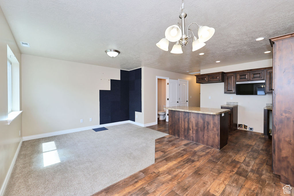 Kitchen with a chandelier, a kitchen island, dark brown cabinets, a textured ceiling, and baseboards