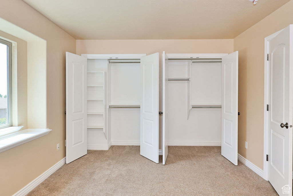 Unfurnished bedroom with light carpet, multiple closets, and baseboards