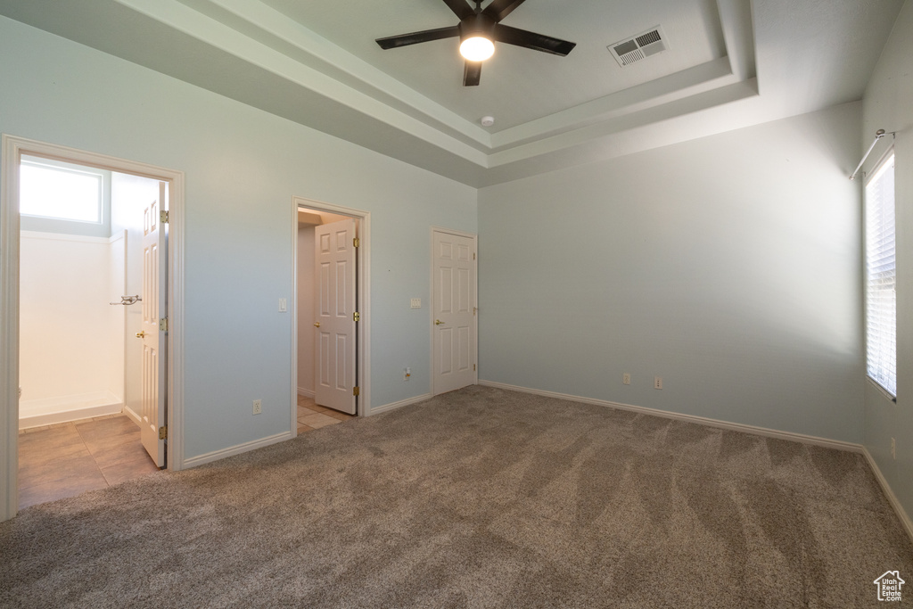 Unfurnished bedroom featuring carpet floors, baseboards, a raised ceiling, and ensuite bathroom